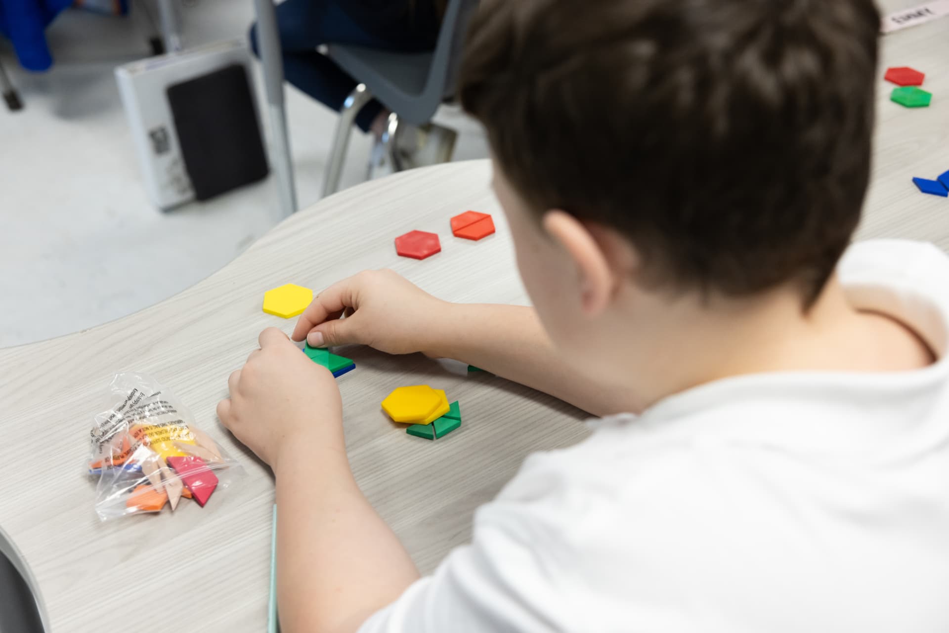 A student creating a design with colorful pattern blocks at a classroom table